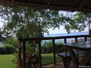 A wooden deck with a table and chairs overlooking a body of water, surrounded by lush greenery.