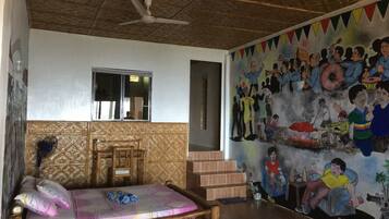 Relax in a traditional room with a bamboo-framed bed and colorful bedspread, surrounded by a lively mural.