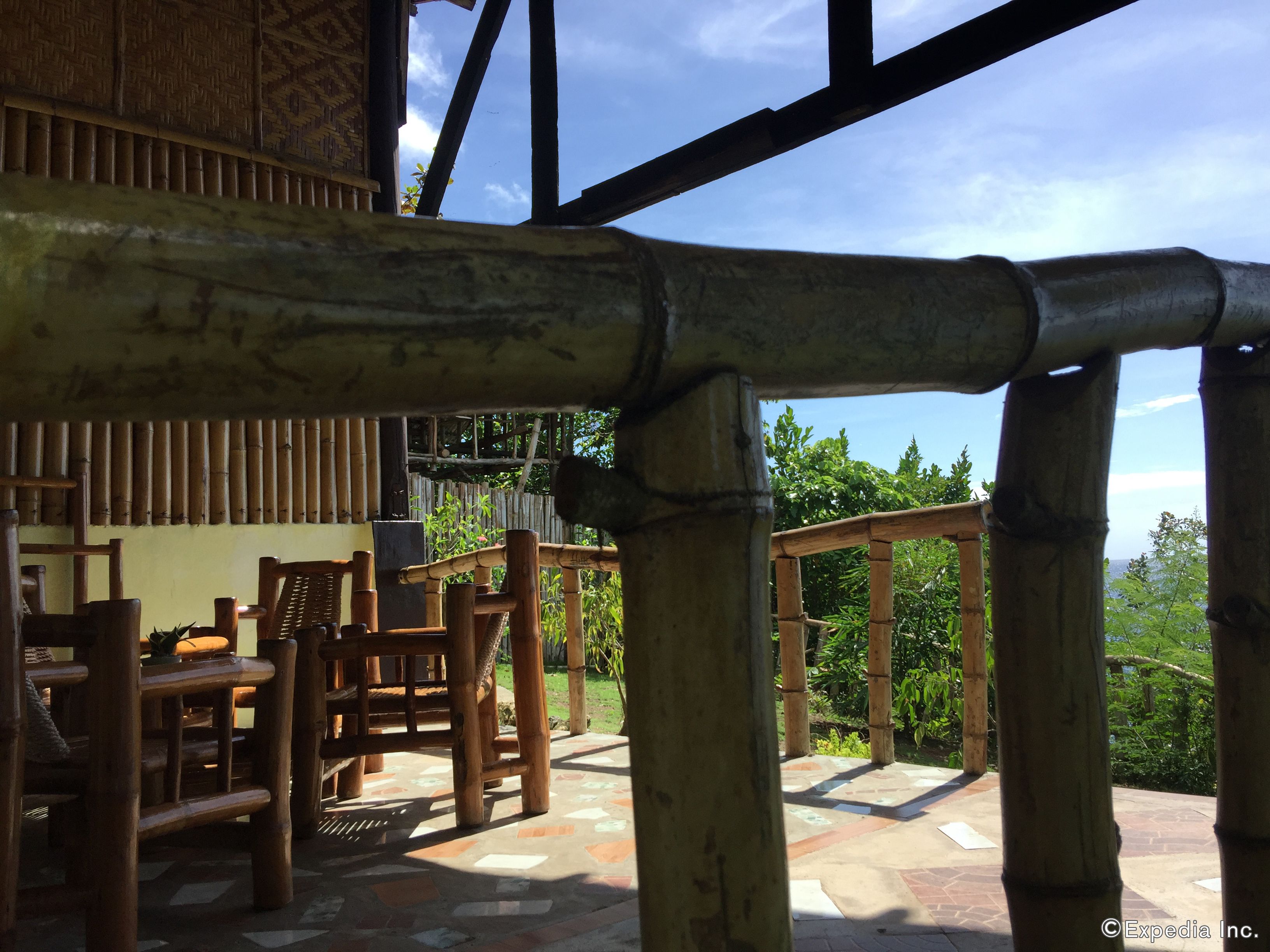 Un área de estar al aire libre con estructura de bambú, con sillas y una mesa, con vista a un jardín y un cielo despejado.