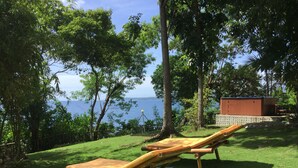 Two wooden lounge chairs on a grassy area with a view of the sea and a wooden structure in the background. - Bohol Lahoy Dive Resort (Guindulman)