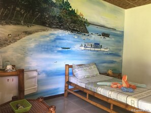 A bedroom with a mural of a beach scene, a bed, a nightstand, and a green basket.