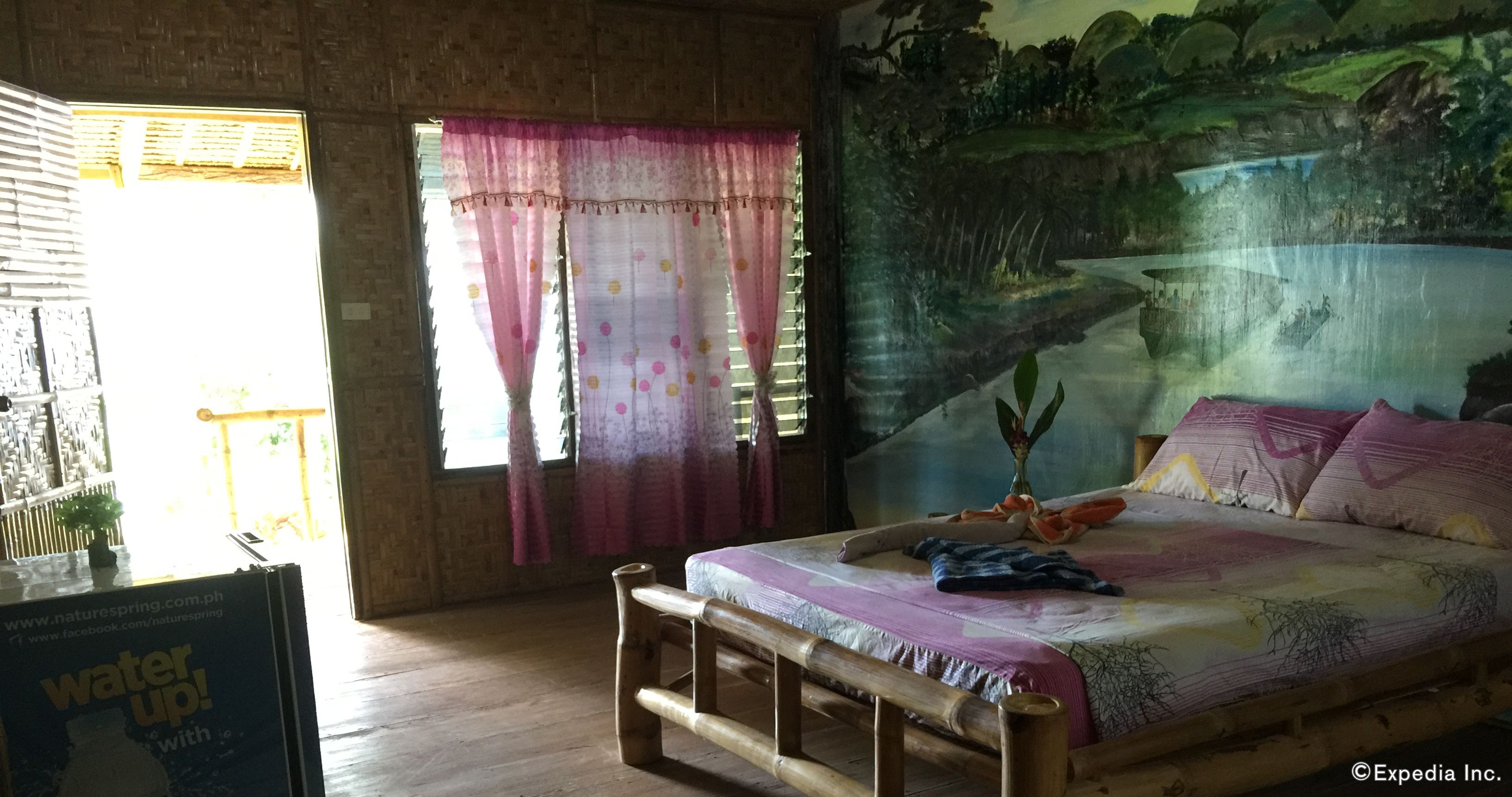 A room with a bed, a wooden bench, a painting on the wall, and a window with curtains.