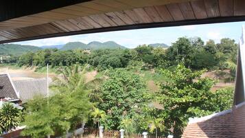 A view from a covered balcony overlooking a lush landscape with trees and distant hills.