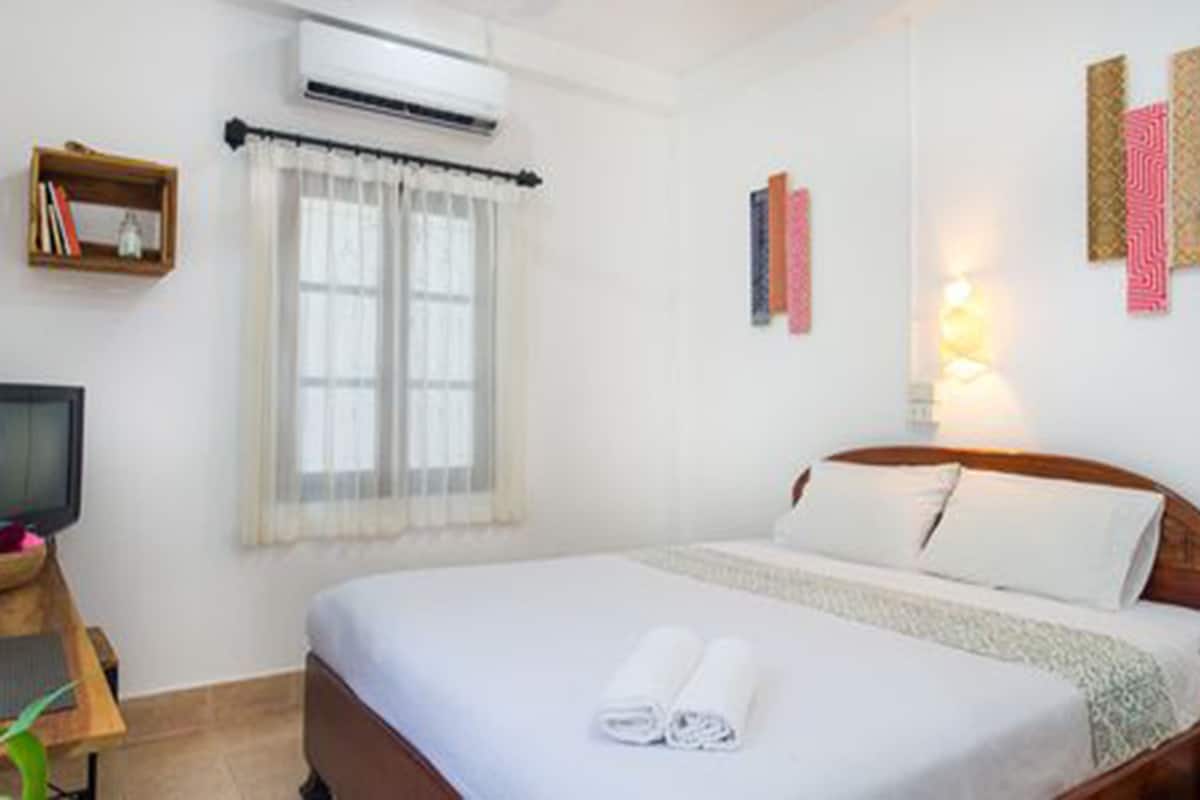 A neatly arranged hotel room with a bed, a desk with a computer, a window with curtains, and wall-mounted artwork.