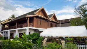 A traditional wooden building with a balcony, surrounded by lush greenery. - Cold River (Luang Prabang)