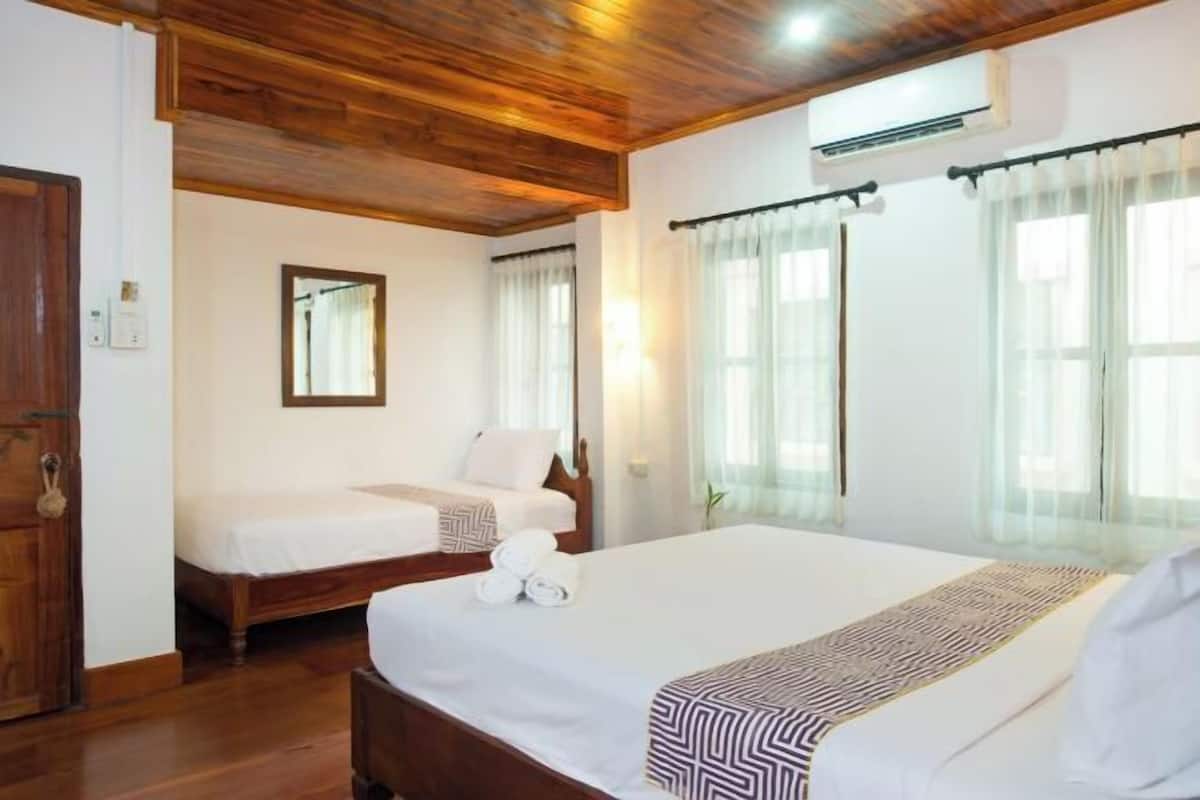 A hotel room with two beds, wooden ceiling, white walls, and a large window with sheer curtains.