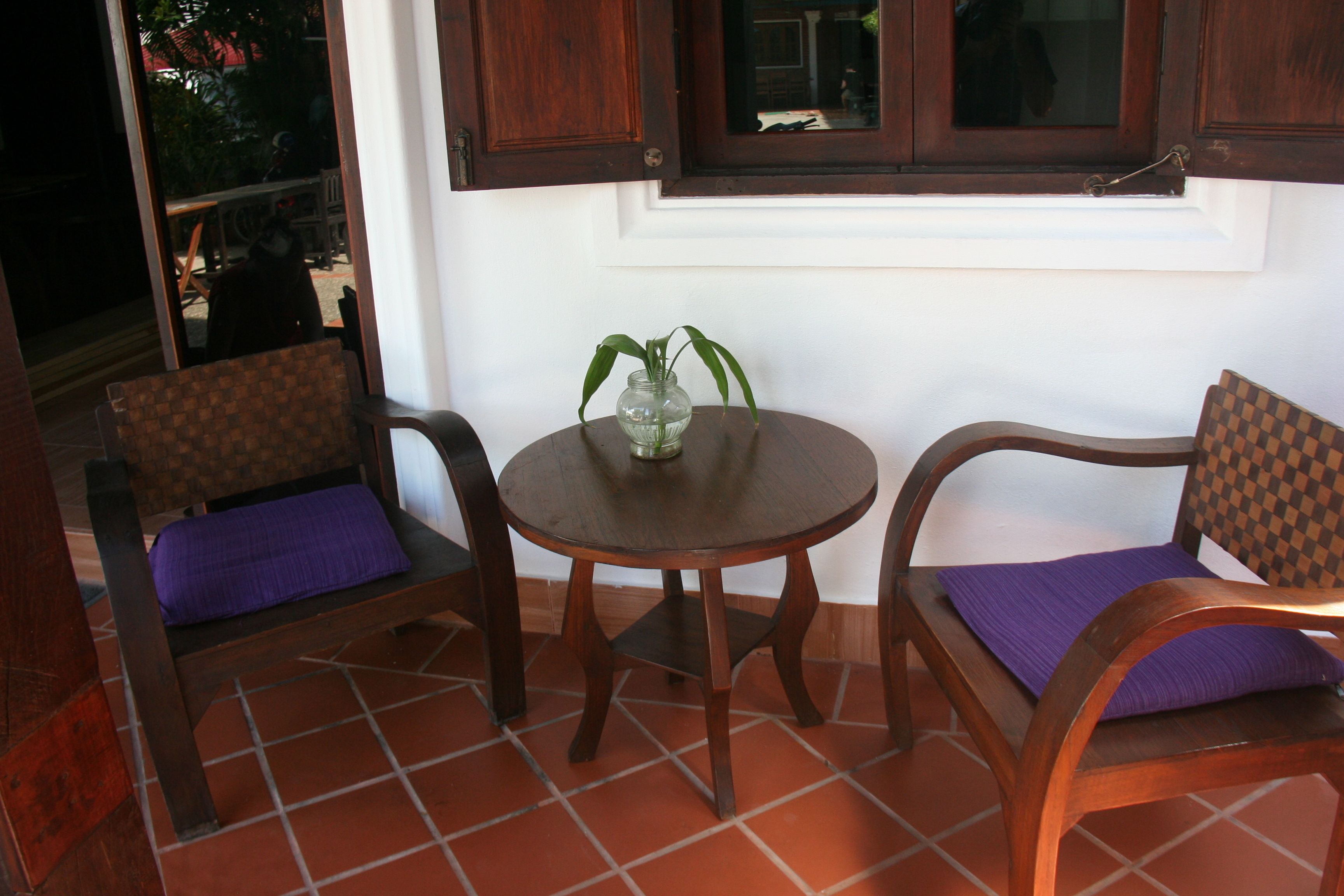 Una habitación con una mesa redonda de madera, dos sillas de madera con cojines morados y una ventana con persianas de madera.