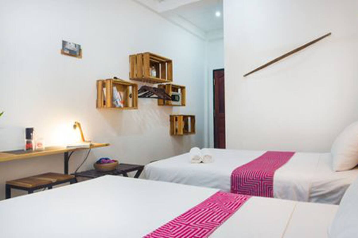 A hotel room with two beds, a bedside table, a lamp, and wooden storage boxes on the wall.