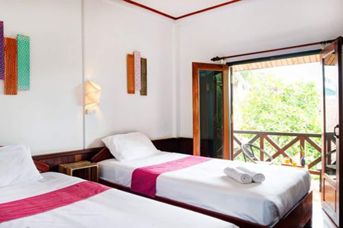 A hotel room with two beds, a balcony, and a view of greenery.