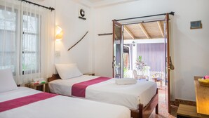 A hotel room with two beds, a window with curtains, a wall-mounted fan, and a sliding door leading to an outdoor area with a chair and table. - Cold River (Luang Prabang)