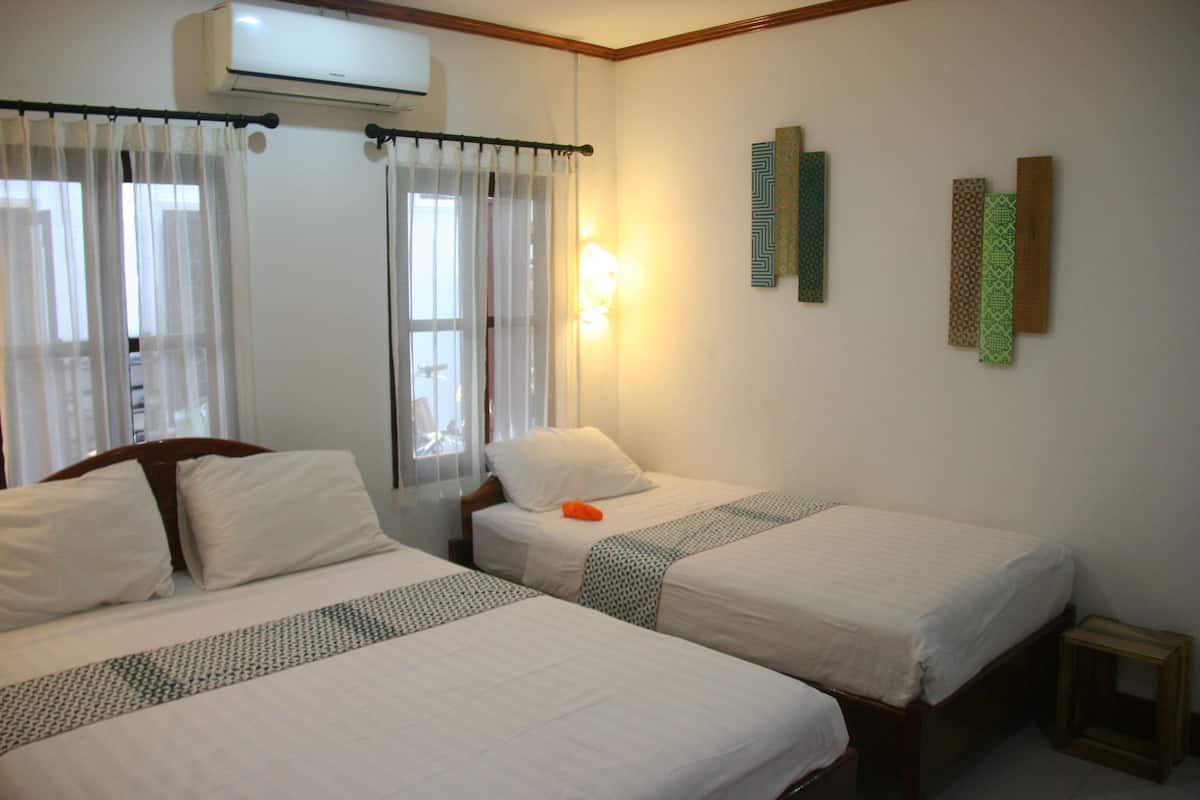 A hotel room with two beds, a window with sheer curtains, an air conditioning unit, and wall-mounted decorative panels.