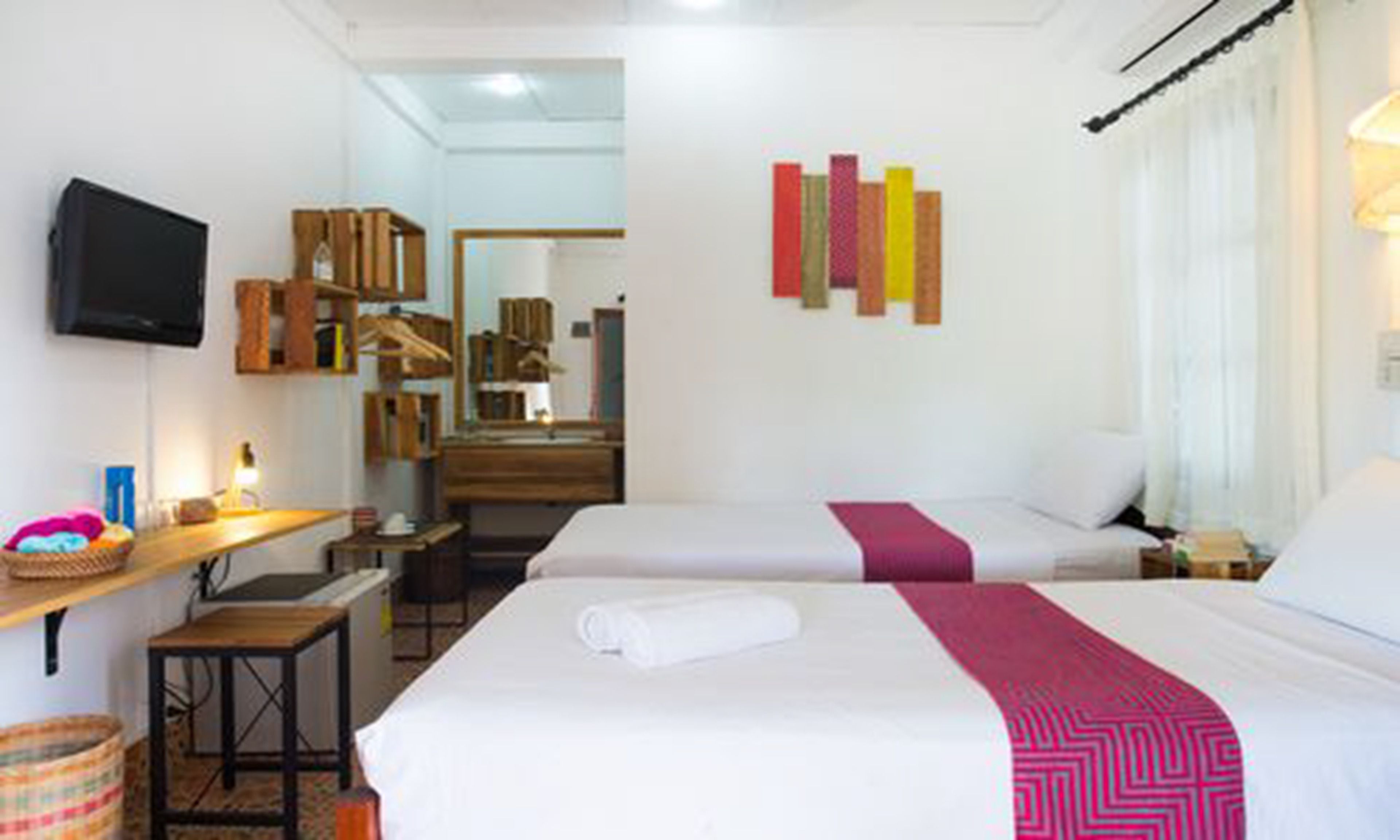 A hotel room with two beds, a desk, a television, and a mirror.