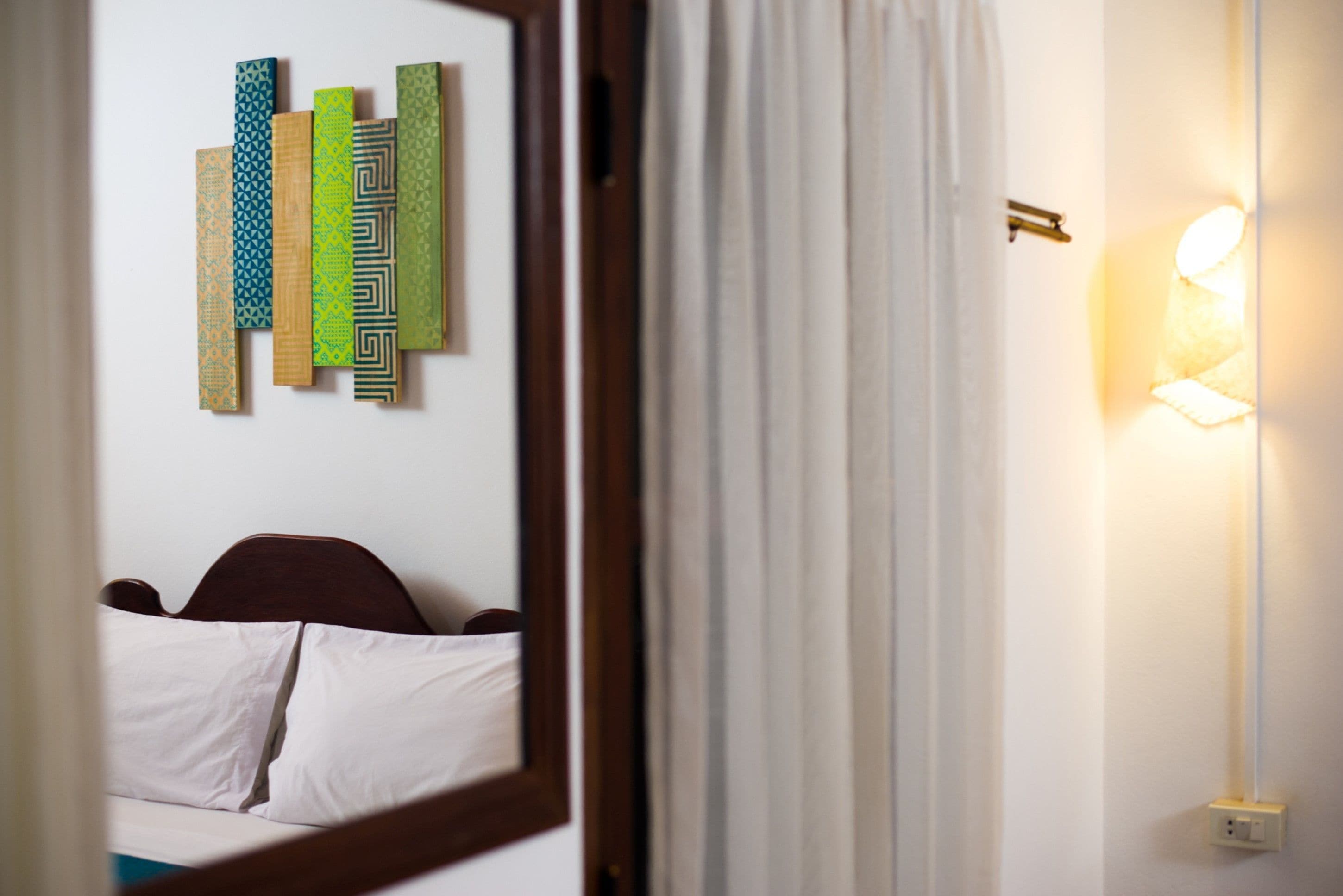 Une chambre d’hôtel avec un lit, un luminaire fixé au mur et un miroir qui reflète la pièce.