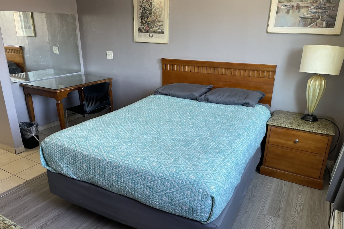 A bedroom with a bed, a desk, a chair, a nightstand, and a lamp.