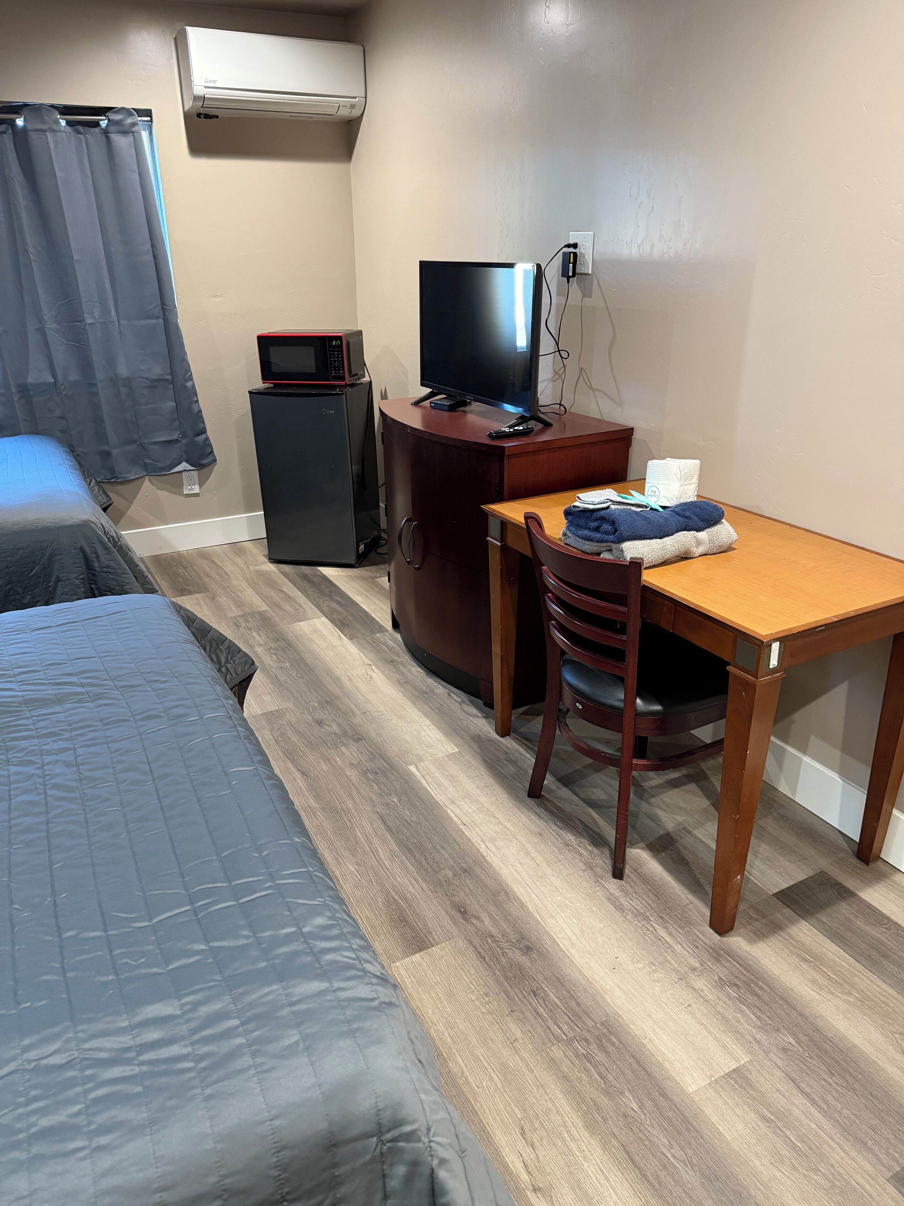 A hotel room with a bed, a desk with a chair, a television, a microwave, and a small refrigerator.
