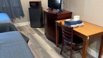 A hotel room with a bed, a desk with a chair, a television, a microwave, and a small refrigerator.