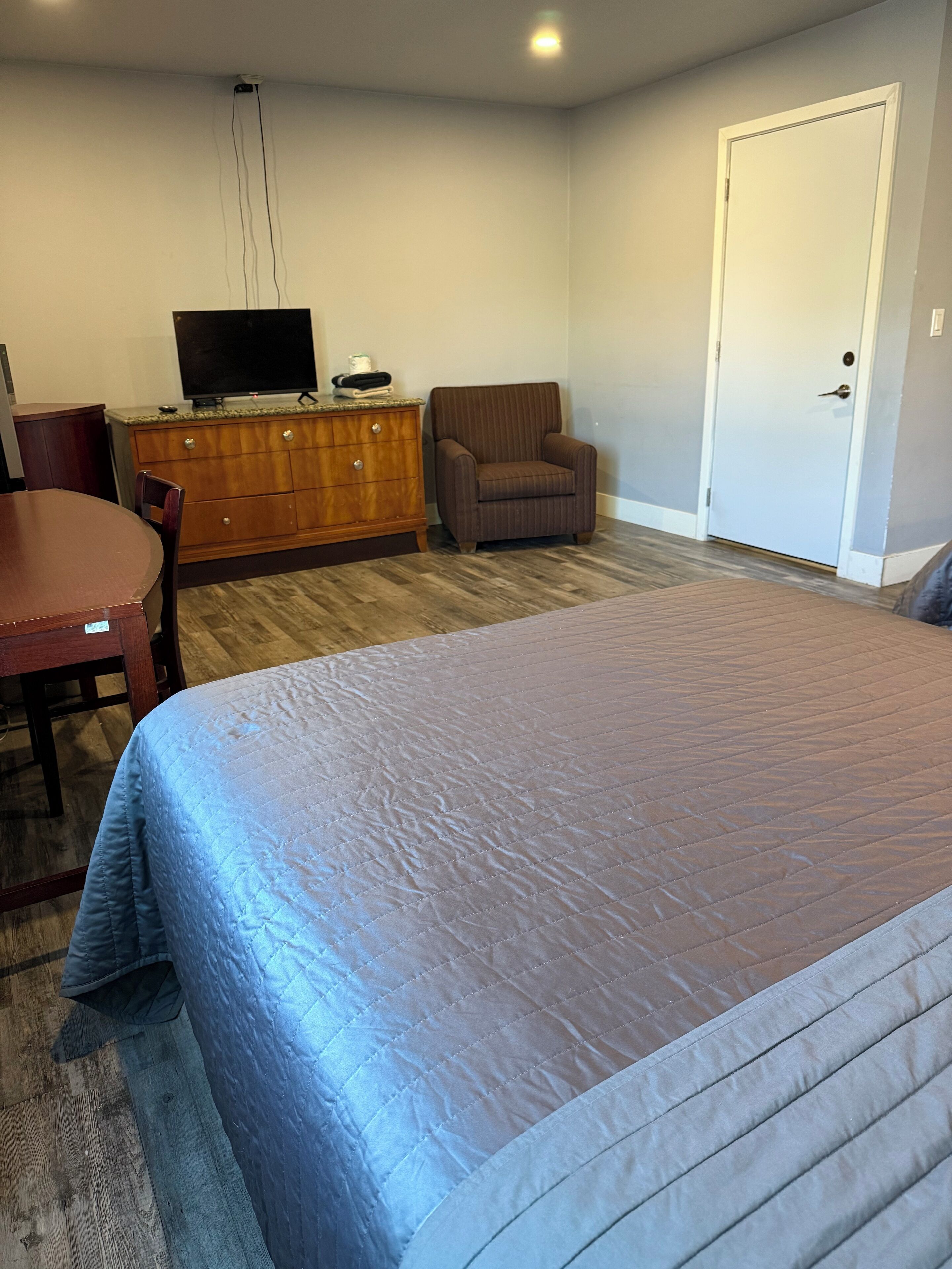 A bedroom with a bed, a wooden dresser, a television, a chair, and a door.
