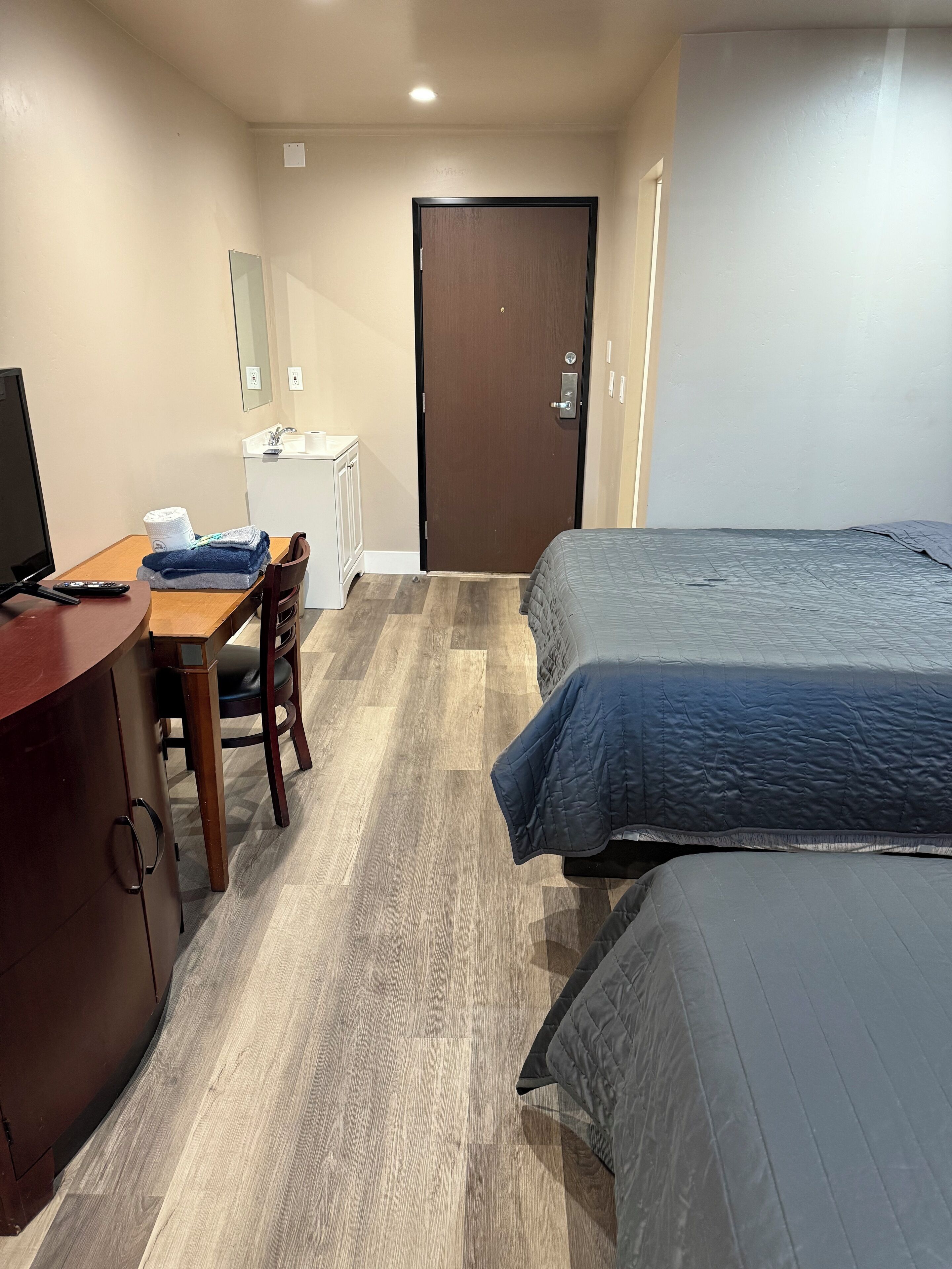 A hotel room with a wooden desk, a bed, a wardrobe, and a door.