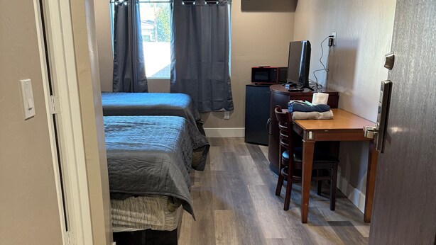 A compact hotel room with two beds, a desk with a computer, a small refrigerator, and an air conditioning unit. - Valley Motel El Cajon-San Diego (El Cajon)