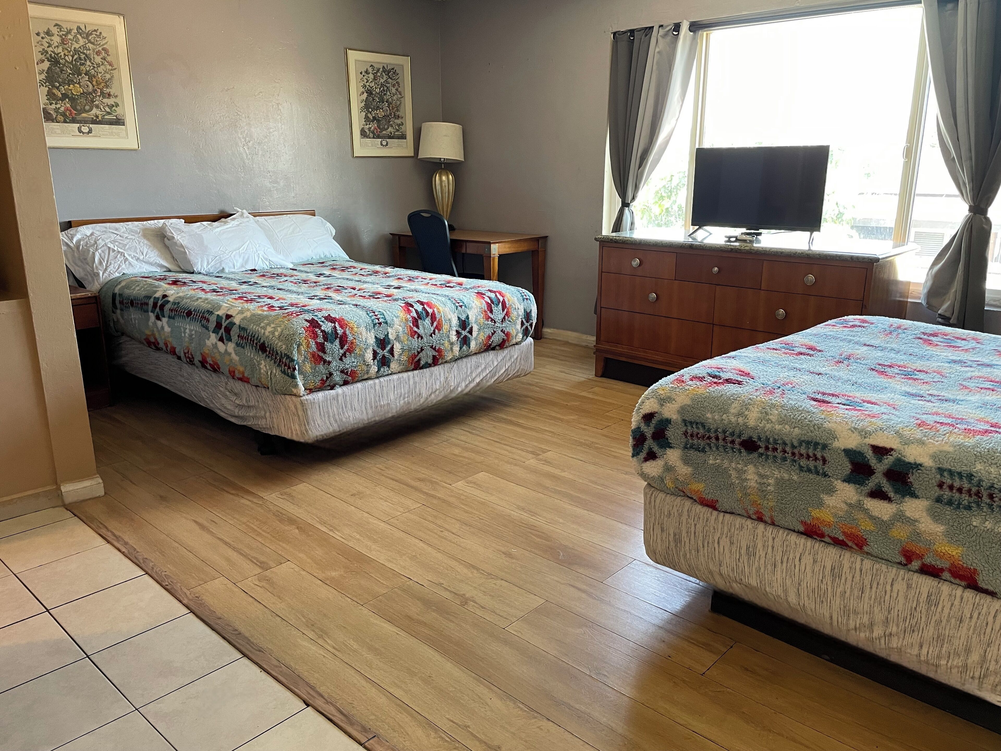 A hotel room with two beds, a wooden dresser, a desk, and a TV.
