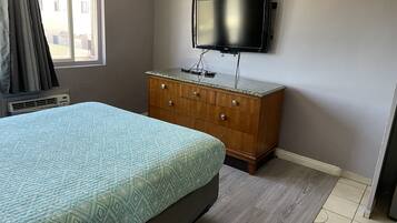 Un dormitorio con cama, cómoda, televisor montado en la pared y ventana con cortinas.