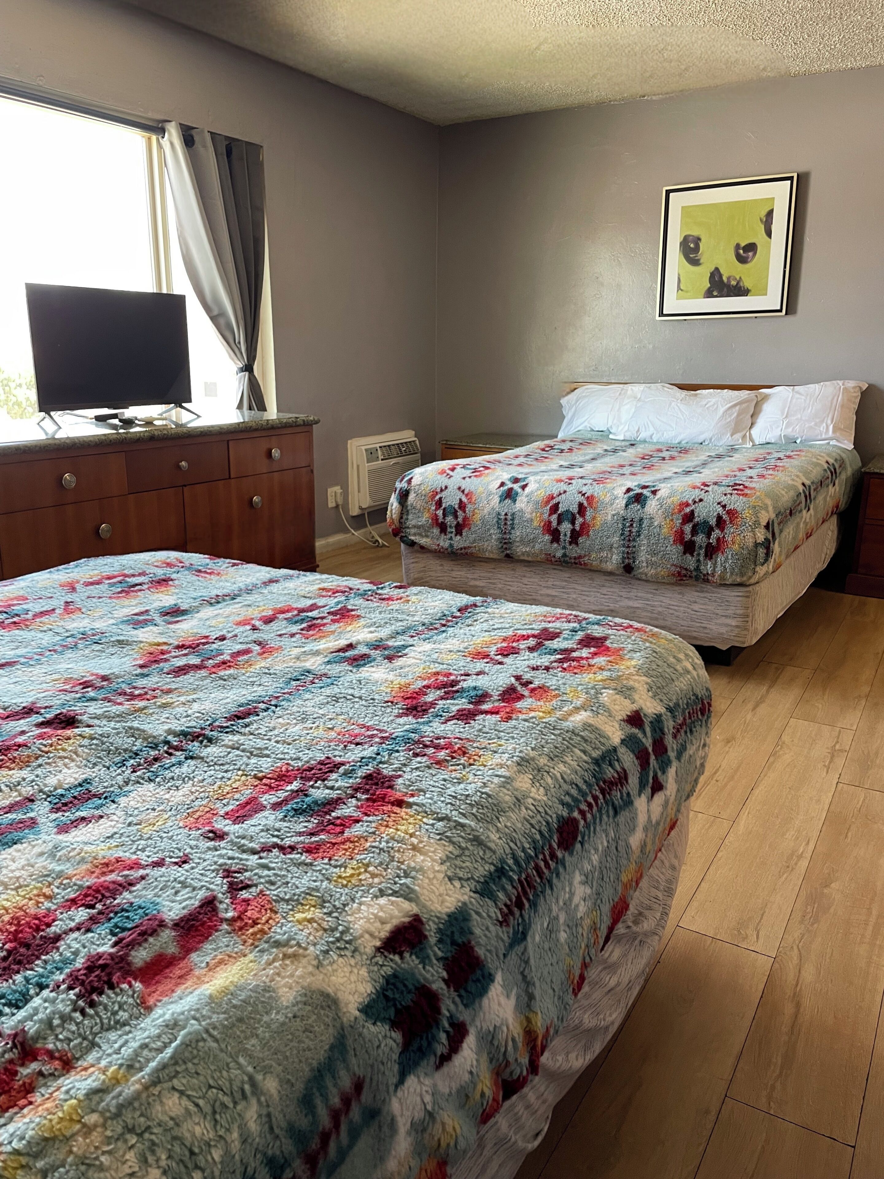A bedroom with two beds, a television on a dresser, and a framed picture on the wall.
