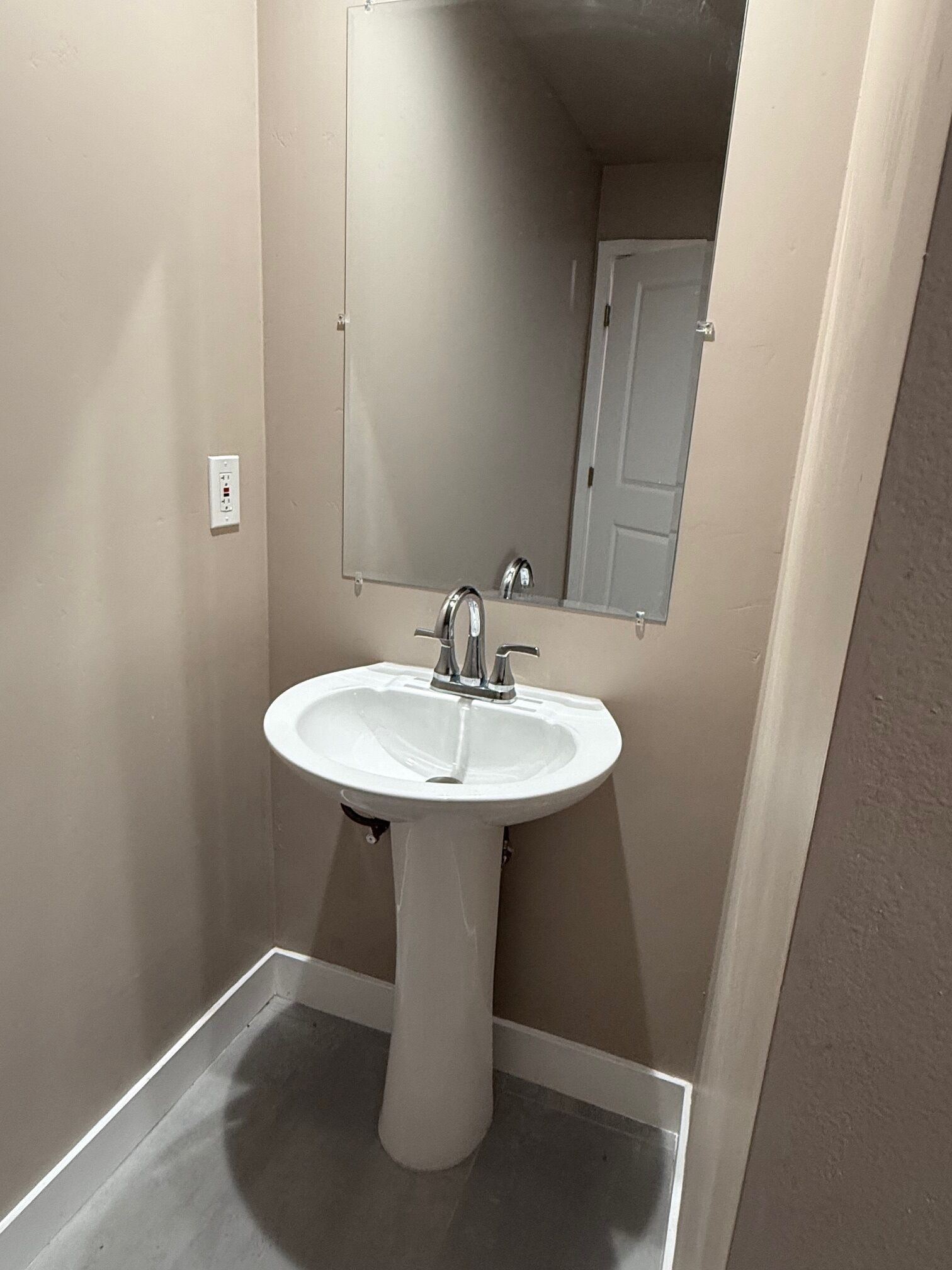 A bathroom with a pedestal sink, a mirror, and a door.