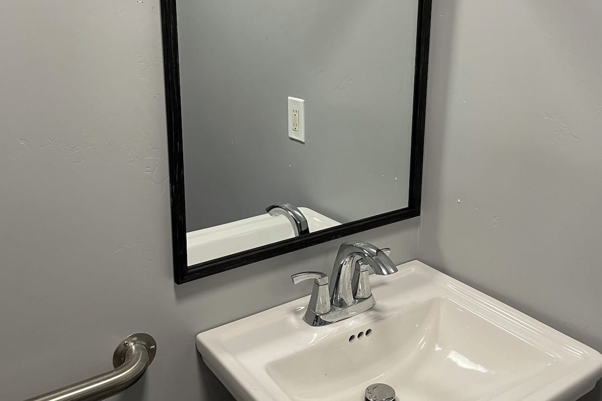 A bathroom with a white sink, a black-framed mirror, and a handrail.