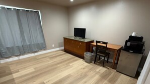 A small, open-plan room with a wooden floor, a desk with a computer, a chair, a television, and a refrigerator. - Valley Motel El Cajon-San Diego (El Cajon)