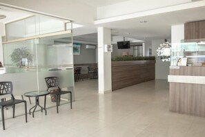 Un hall d’hôtel moderne avec des cloisons en verre, un comptoir d’accueil et des espaces aménagés avec des sièges.