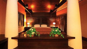 A hotel room with a wooden ceiling, a bed with white linens, two bedside tables with lamps, and a plant on the nightstand. - Panchalae Boutique Residences (Pattaya)