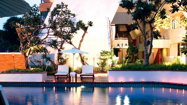 An outdoor pool area with lounge chairs, a tree, and a building in the background. - Panchalae Boutique Residences (Pattaya)