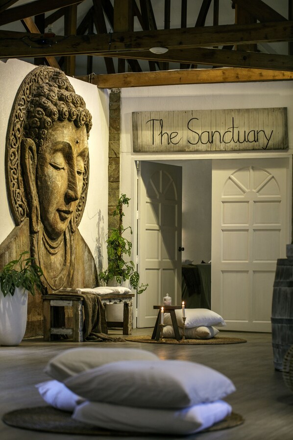 Una habitación con una gran estatua de Buda, un letrero que dice 'The Sanctuary', y un rincón de descanso acogedor con cojines y una pequeña mesa.