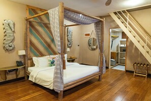 Uma cama com dossel e cortina, uma escrivaninha de madeira com telefone e uma escada que leva a um andar superior.