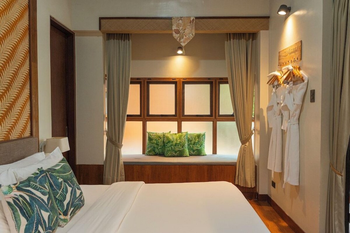 A hotel room with a large bed, a window with curtains, a wall-mounted robe rack, and a decorative headboard.