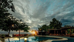 A pool area with a sunset view, lounge chairs, and a covered seating area. - Club Serena Resort (Moalboal)