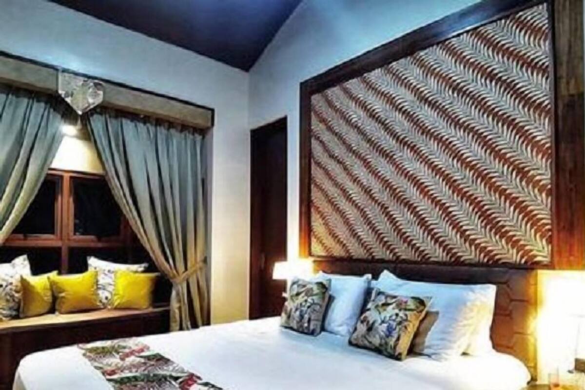 A bedroom with a bed, pillows, curtains, and a patterned headboard.