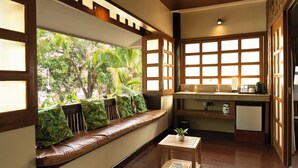 A room with a wooden bench with cushions, a small table with a plant, and a kitchen area with a refrigerator and sink. - Club Serena Resort (Moalboal)