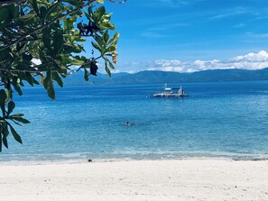 Una playa con agua cristalina, un bote y montañas a lo lejos.