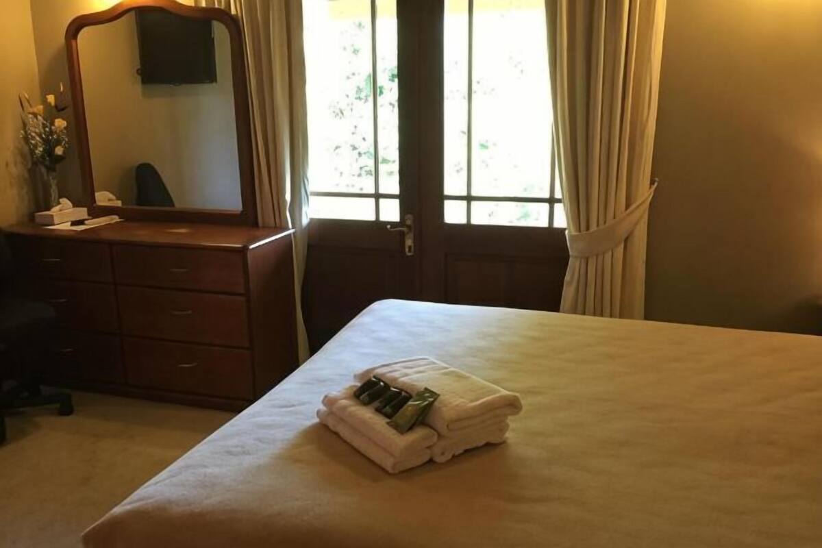 Een hotelkamer met een bed, een dressoir, een spiegel en een raam met gordijnen.