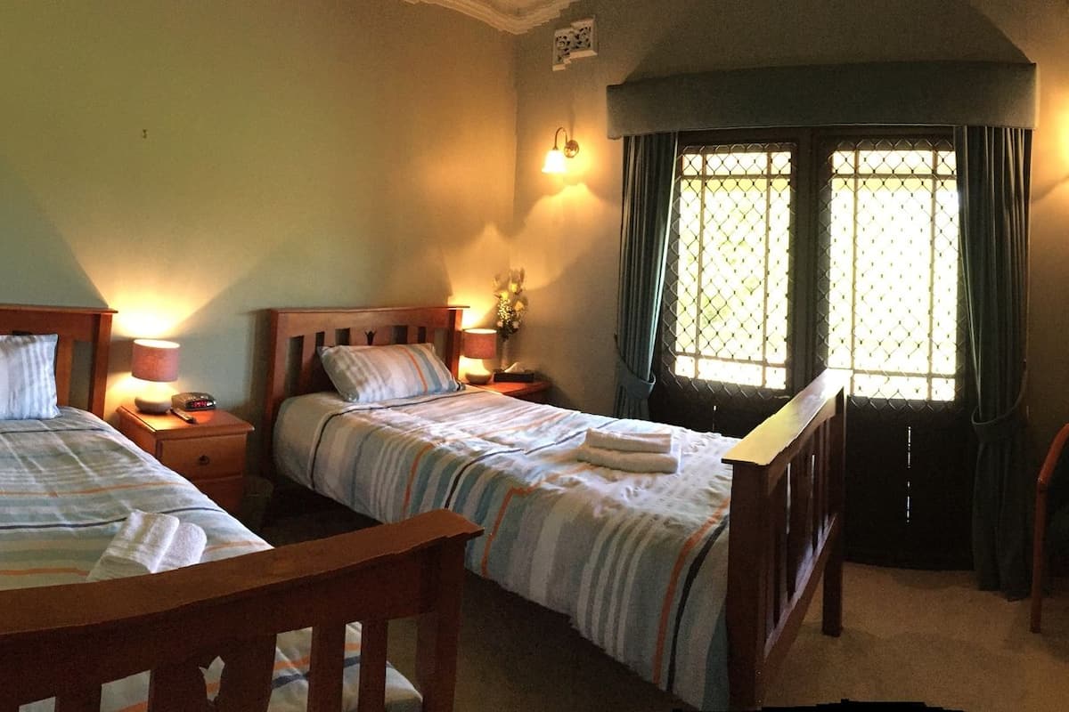 Een slaapkamer met twee bedden, een stoel, een televisie en een deur naar een andere kamer.