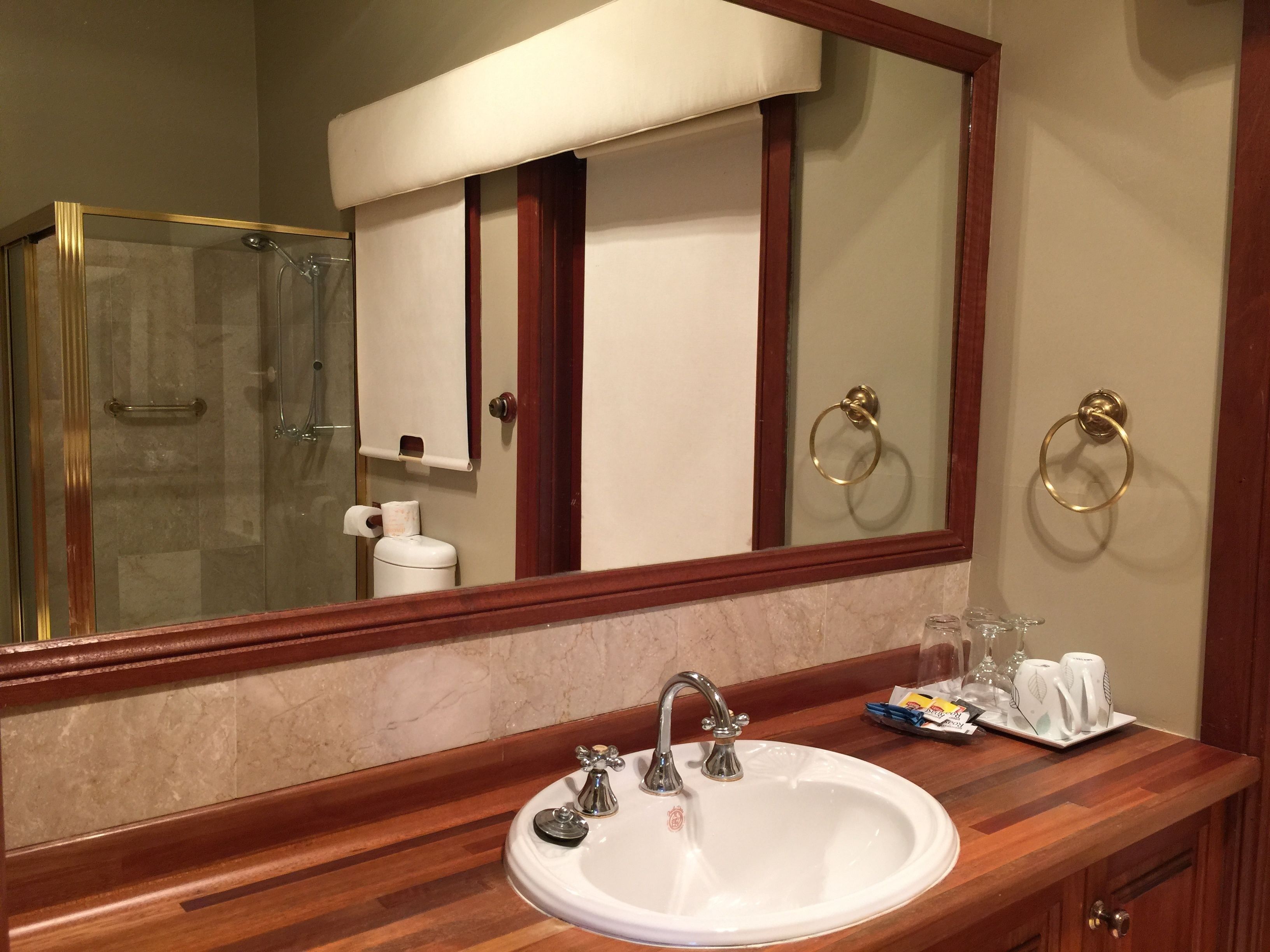 A bathroom with a white sink, a glass shower enclosure, a mirror with a wooden frame, and a towel rack.