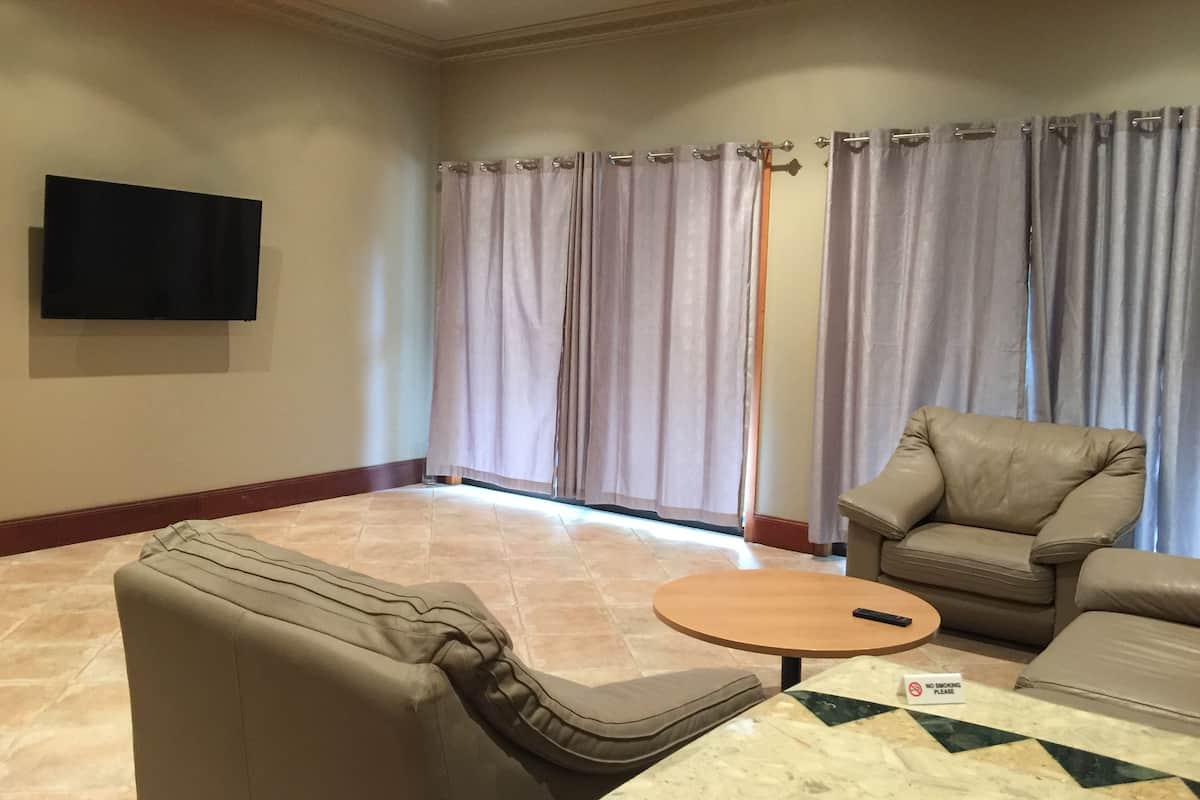 Een woonkamer met een flatscreen televisie aan de muur, een beige bank, een ronde salontafel en een bordje ‘Niet roken’ op de vloer.