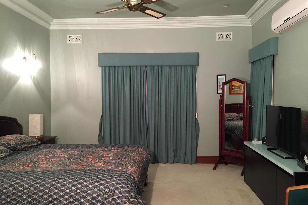 Een slaapkamer met een bed, een dressoir, een televisie en een plafondventilator.