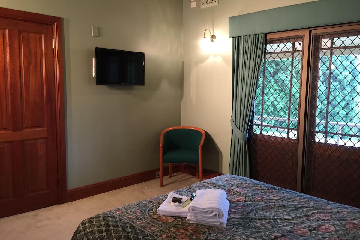 Een hotelkamer met een bed, een televisie, een stoel en een raam met gordijnen.