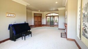 A spacious room with a piano, a large painting, and a wooden door leading to an outdoor area. - Relaxin (Middle Dural)