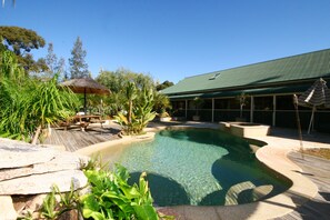 A swimming pool with a curved edge, surrounded by a wooden deck and lush greenery. - Relaxin (Middle Dural)