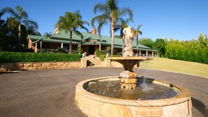 A landscaped area with a fountain, palm trees, and a building with a green roof. - Relaxin (Middle Dural)
