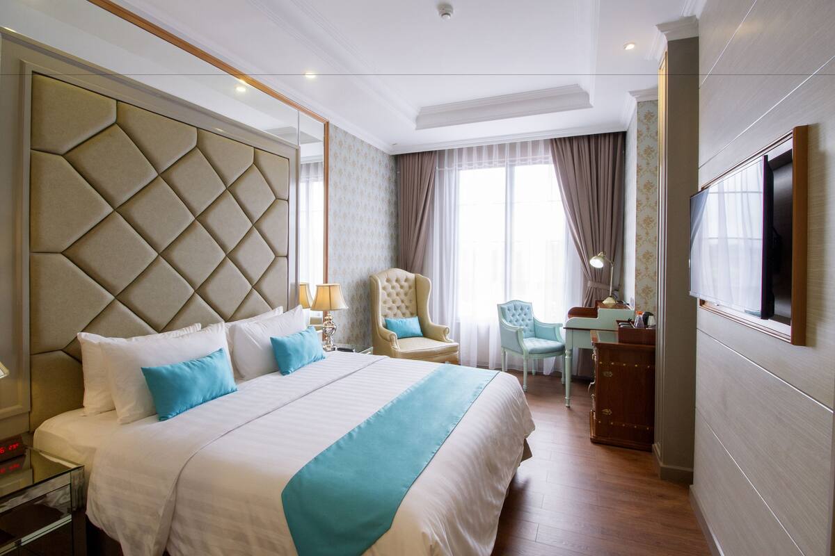 Ein Hotelzimmer mit einem großen Bett, einem Schreibtisch, einem Sessel und einem Fernseher.