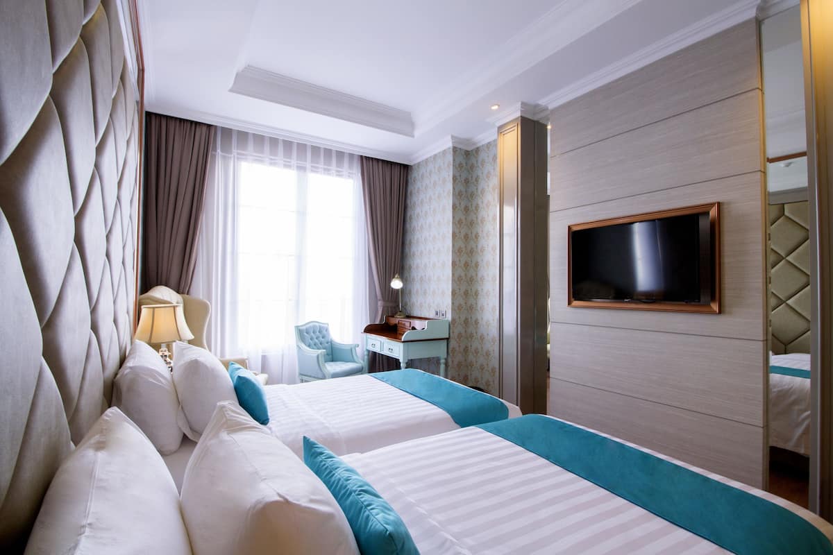 Ein Hotelzimmer mit zwei Betten, einem Fernseher, einem Schreibtisch und einem Sessel.